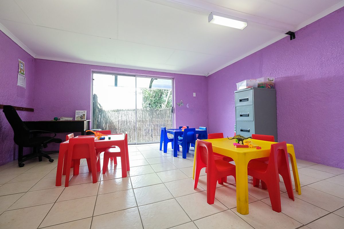 A classroom with purple walls, an upright piano and low tables set with chairs