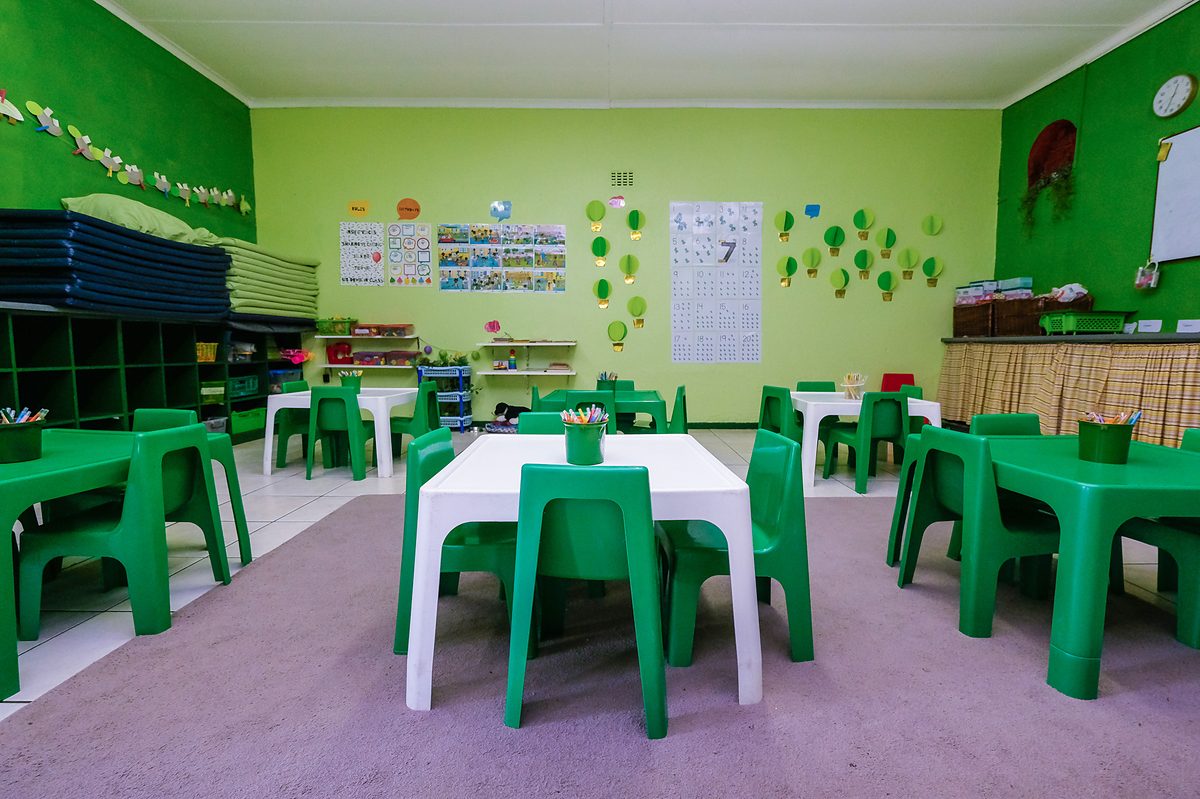 Green Class: green walls, green tables and chairs, with stacked mats and storage along the wall