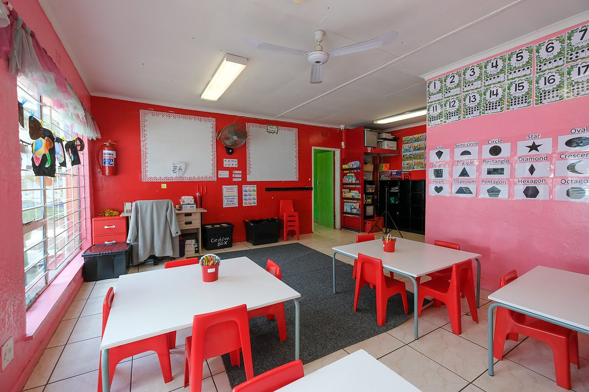 Red Class: red and pink walls with alphabet and number charts, red tables and chairs, and a whiteboard