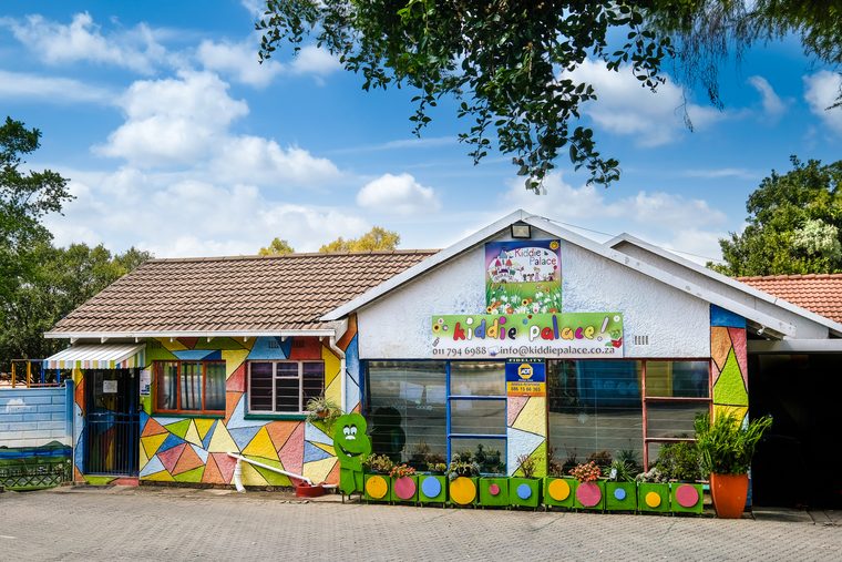 The front of the school: a brightly painted building with the Kiddie Palace name above the windows and colourful flower boxes along the path