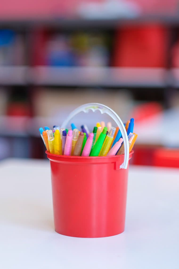 A red bucket of coloured pencils on a white table