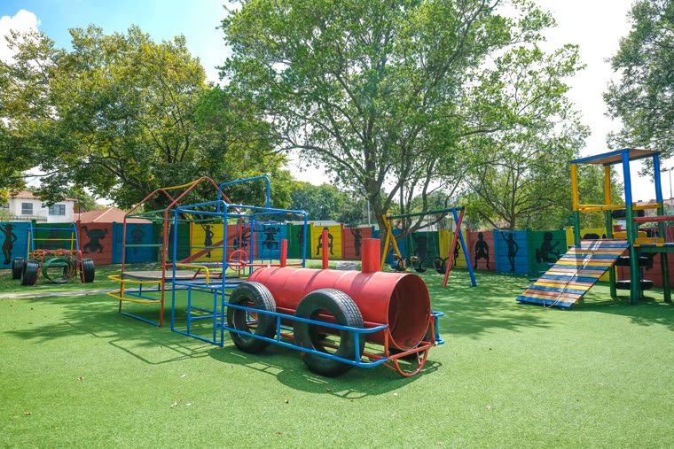 The main playground: a climbing frame, tunnel and slide on artificial lawn, with painted silhouettes along the boundary wall