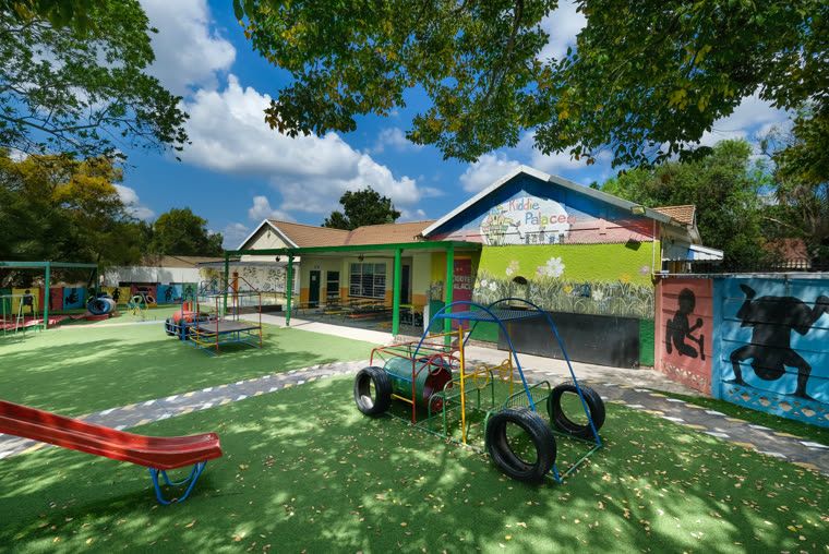 A wide view of the playground with a see-saw and tyres, the school buildings behind