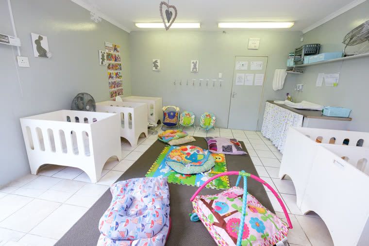 The infant room: white cots along the wall, with play mats and baby gyms on the floor
